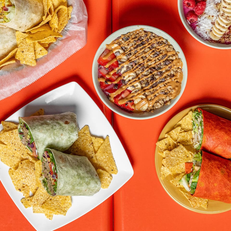 Assortment of healthy wraps with tortilla chips and colorful acai bowls on an orange background.
