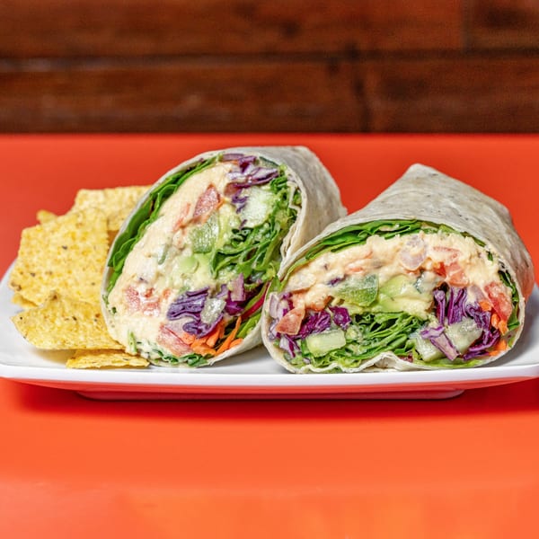 Two healthy Raw Addiction Plus wraps, filled with fresh vegetables and hummus, served with tortilla chips.