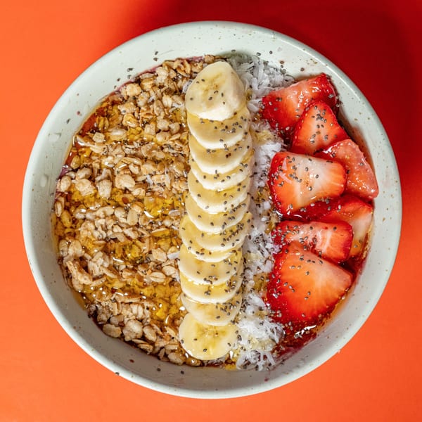 Overhead view of a Raw Addiction Plus acai bowl with granola, bananas, coconut, and strawberries.