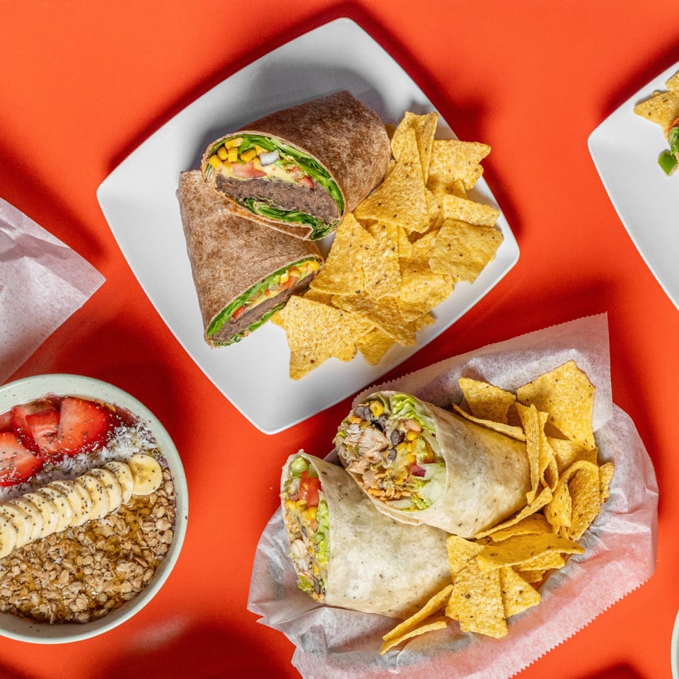 Two healthy wraps with tortilla chips and a fruit and granola bowl on a red background.